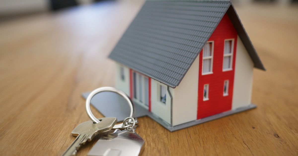 Model house and silver keys on a wooden table